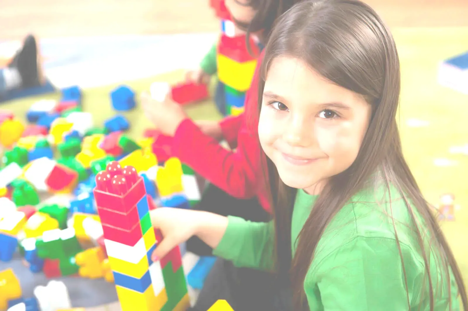 A smiling girl in a green top building a tall tower from bright plastic blocks